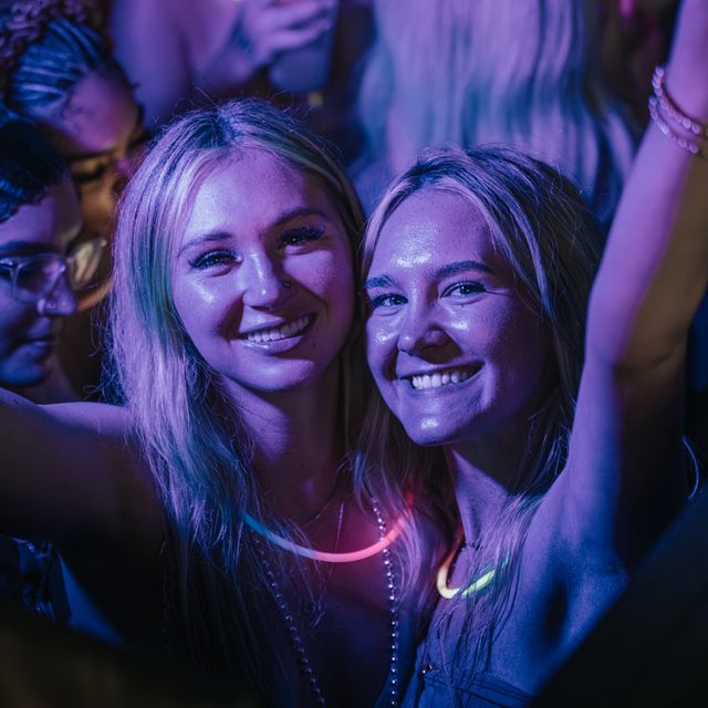 Two friends smiling with glow necklaces at a PCB Spring Break 2026 party